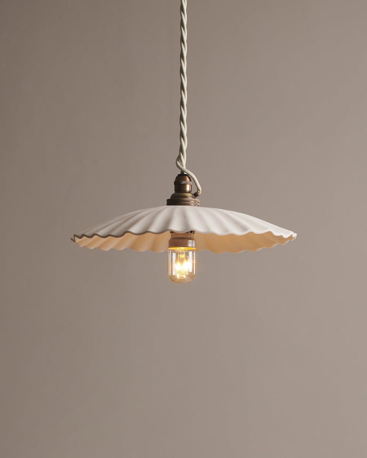 A large narrow pleat porcelain pendant light with an unglazed finish, an aged brass B22 lampholder and a white twisted fabric flex cord. TEST