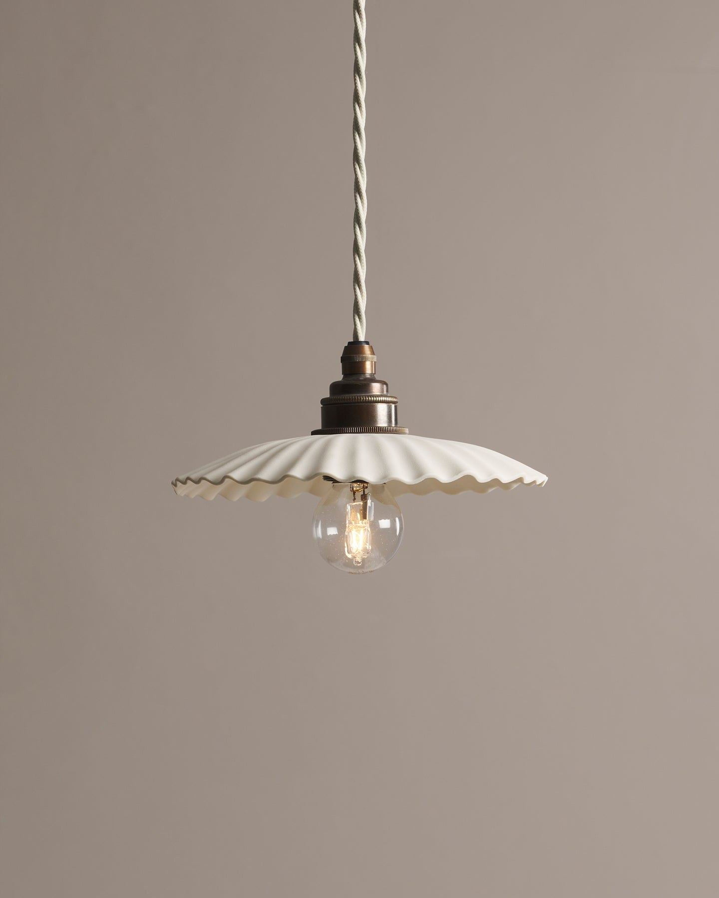 A small narrow pleat porcelain pendant light with an unglazed finish, an aged brass E27 lampholder and a white twisted fabric flex cord.