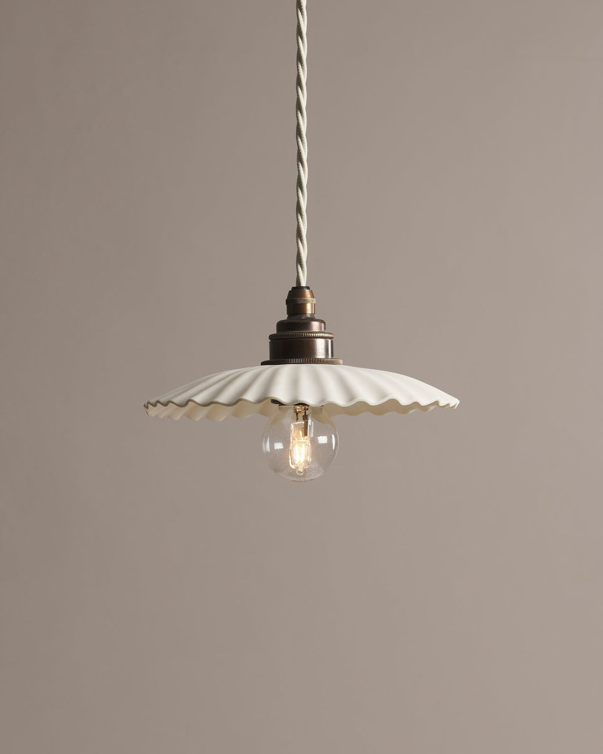 A small narrow pleat porcelain pendant light with an unglazed finish, an aged brass E27 lampholder and a white twisted fabric flex cord. TEST