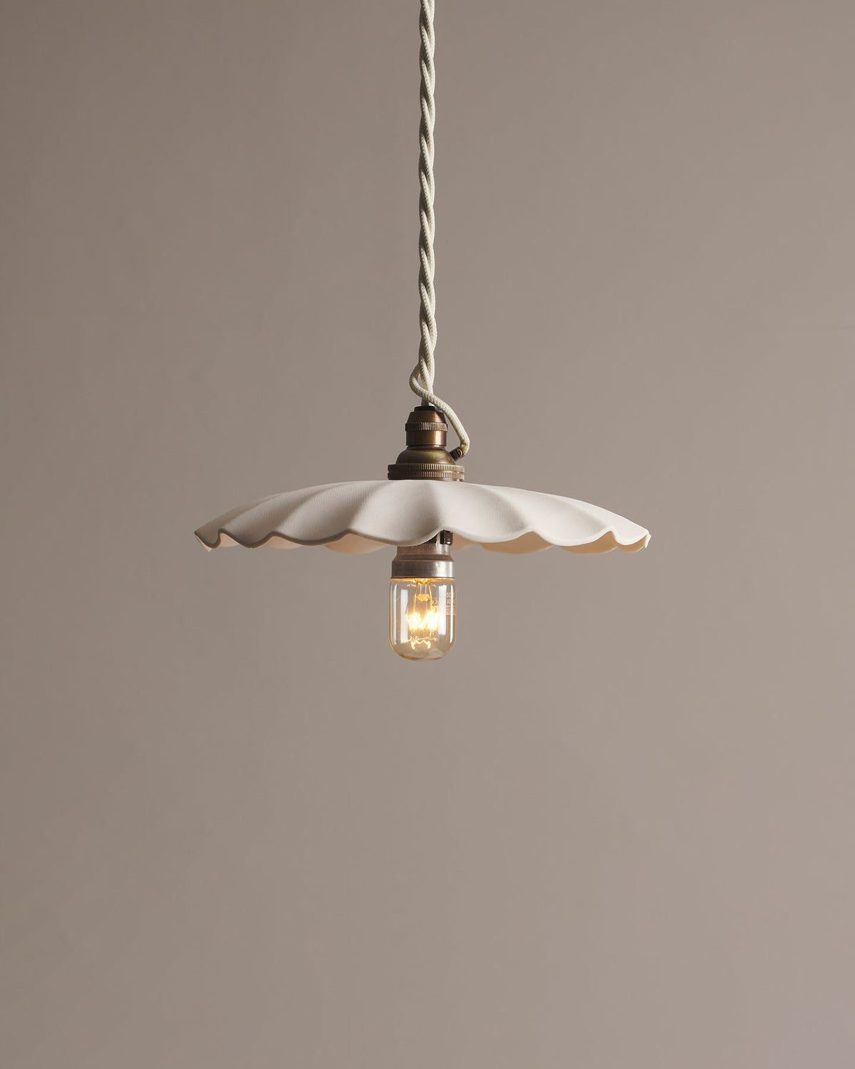 A large wide pleat porcelain pendant light with an unglazed finish, an aged brass B22 lampholder and a white twisted fabric flex cord. TEST