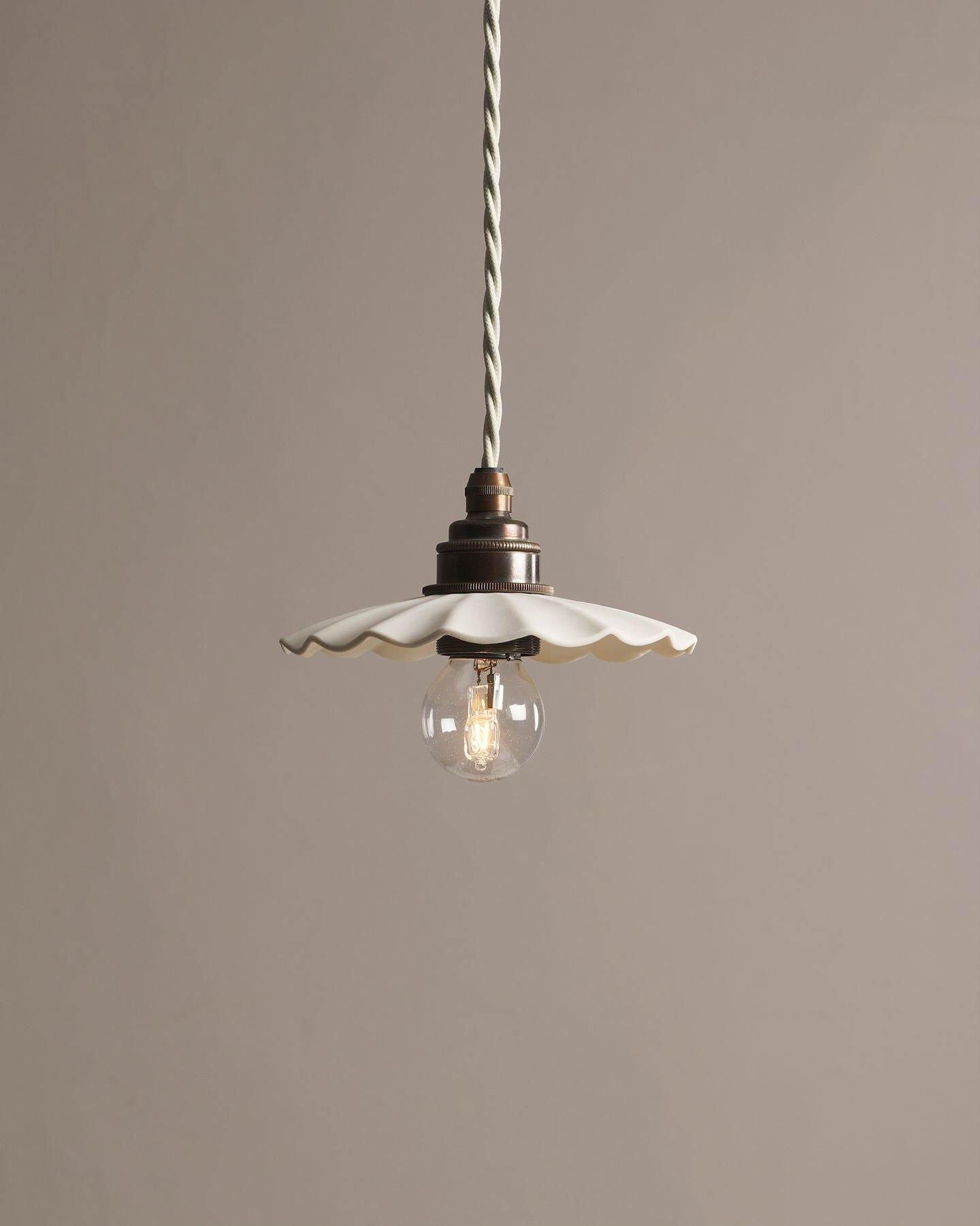 A small wide pleat porcelain pendant light with an unglazed finish, an aged brass E27 lampholder and a white twisted fabric flex cord.
