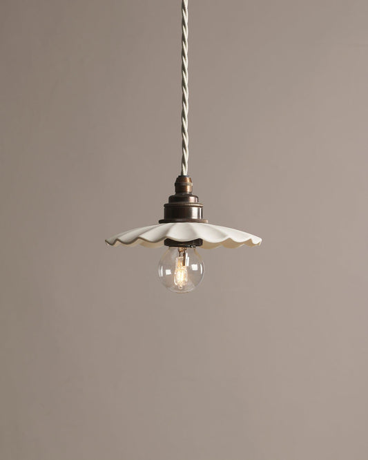 A small wide pleat porcelain pendant light with an unglazed finish, an aged brass E27 lampholder and a white twisted fabric flex cord.