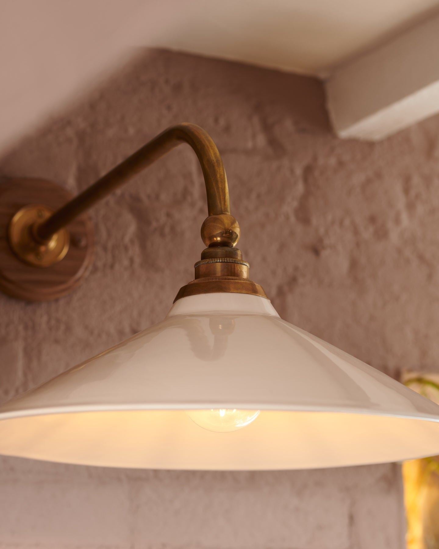 A close-up view of a large Victorian-inspired wall light with a brass arm and a cream glazed ceramic shade.