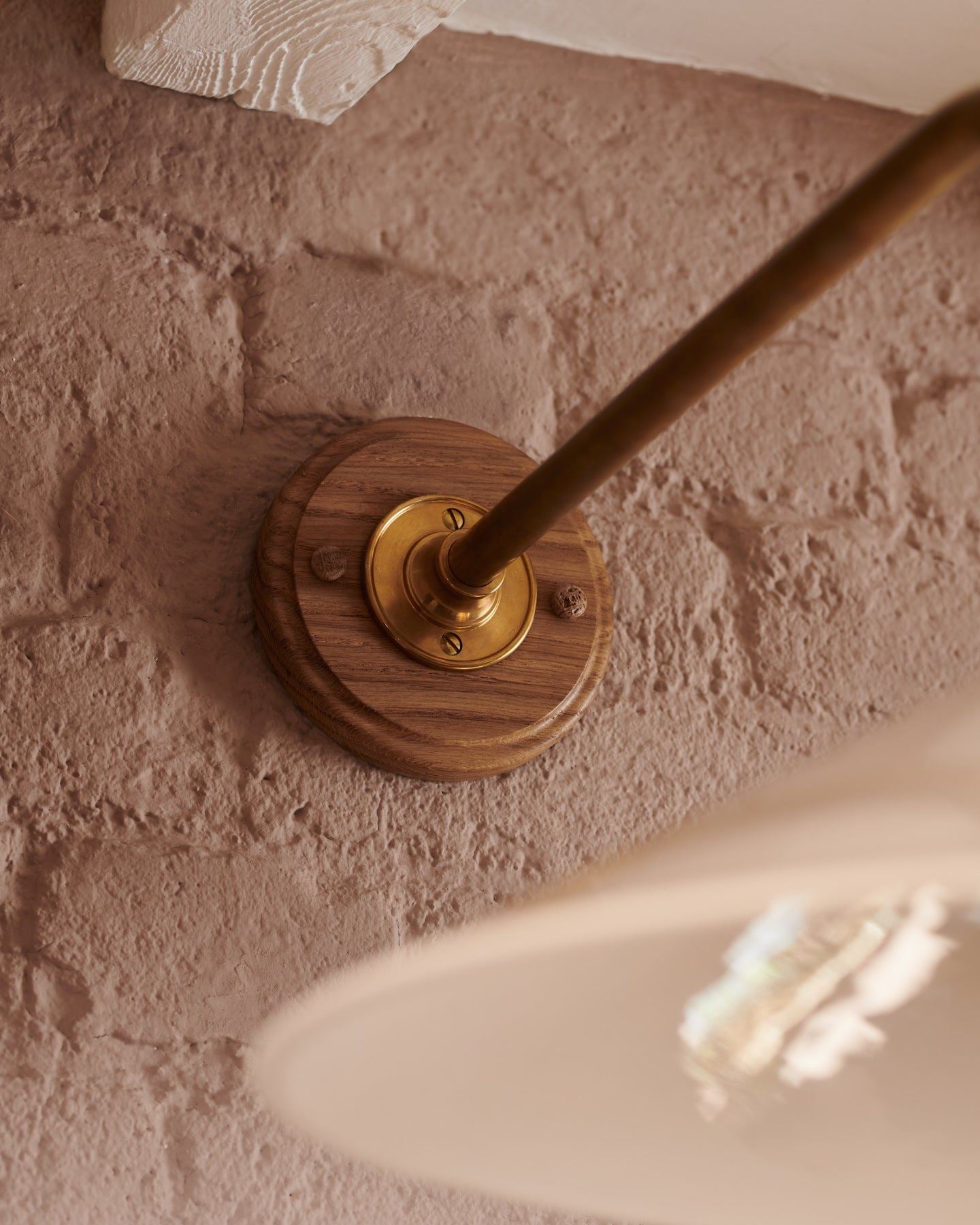 A close-up view of the oak pattress and brass arm of a large Victorian-inspired wall light.