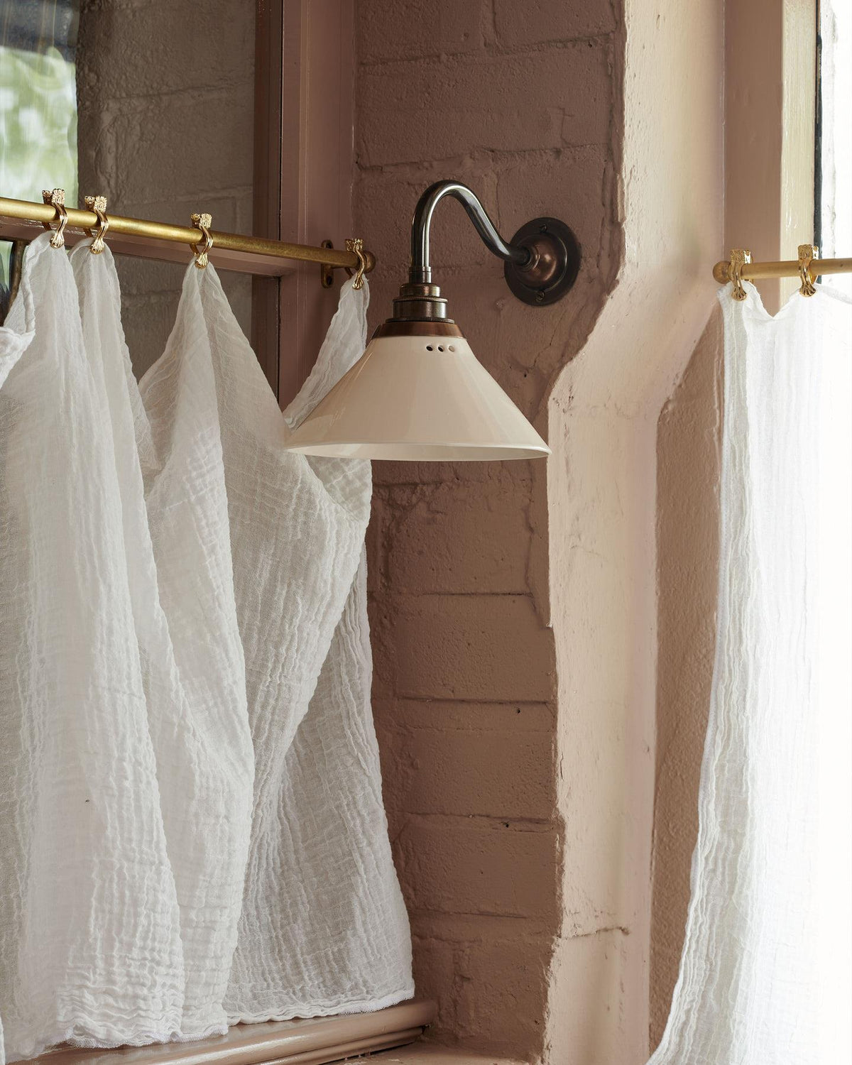 An atmospheric cottage room with pink brick walls, beamed ceiling and small wall lights either side of a window. TEST