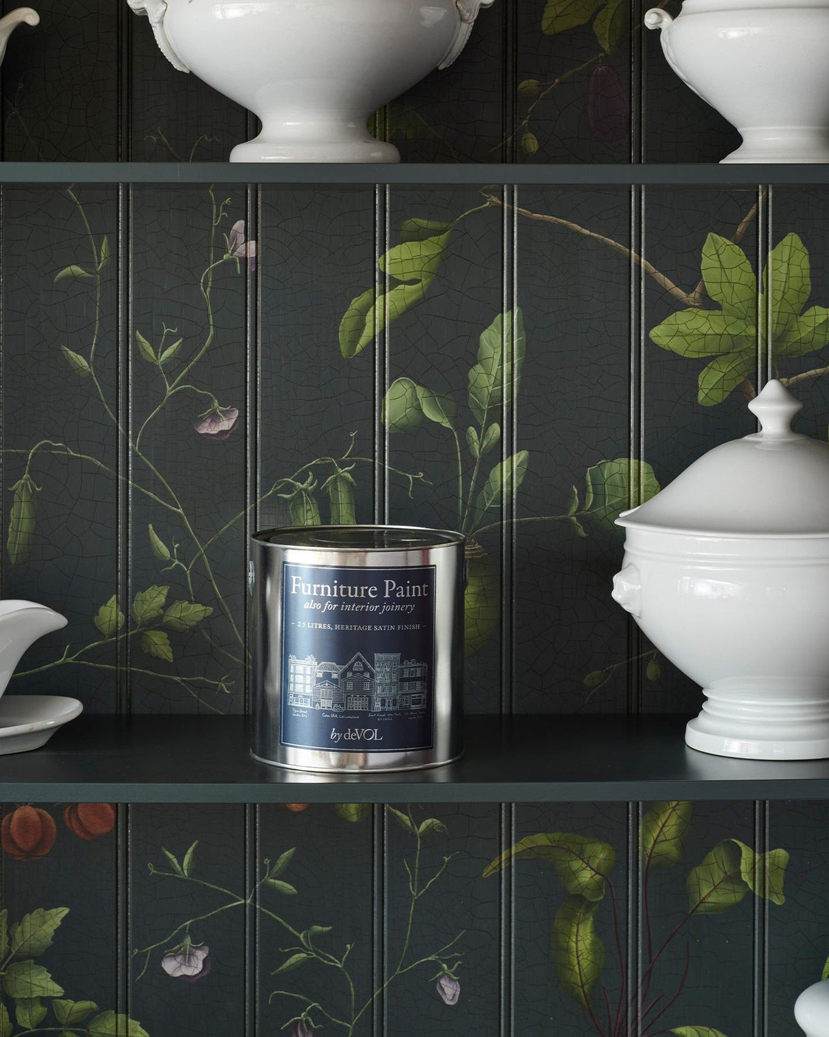 A silver paint tin with a rich blue label inside a dark green cupboard interior with hand-painted botanical flora on a tongue and groove-style backboard. TEST