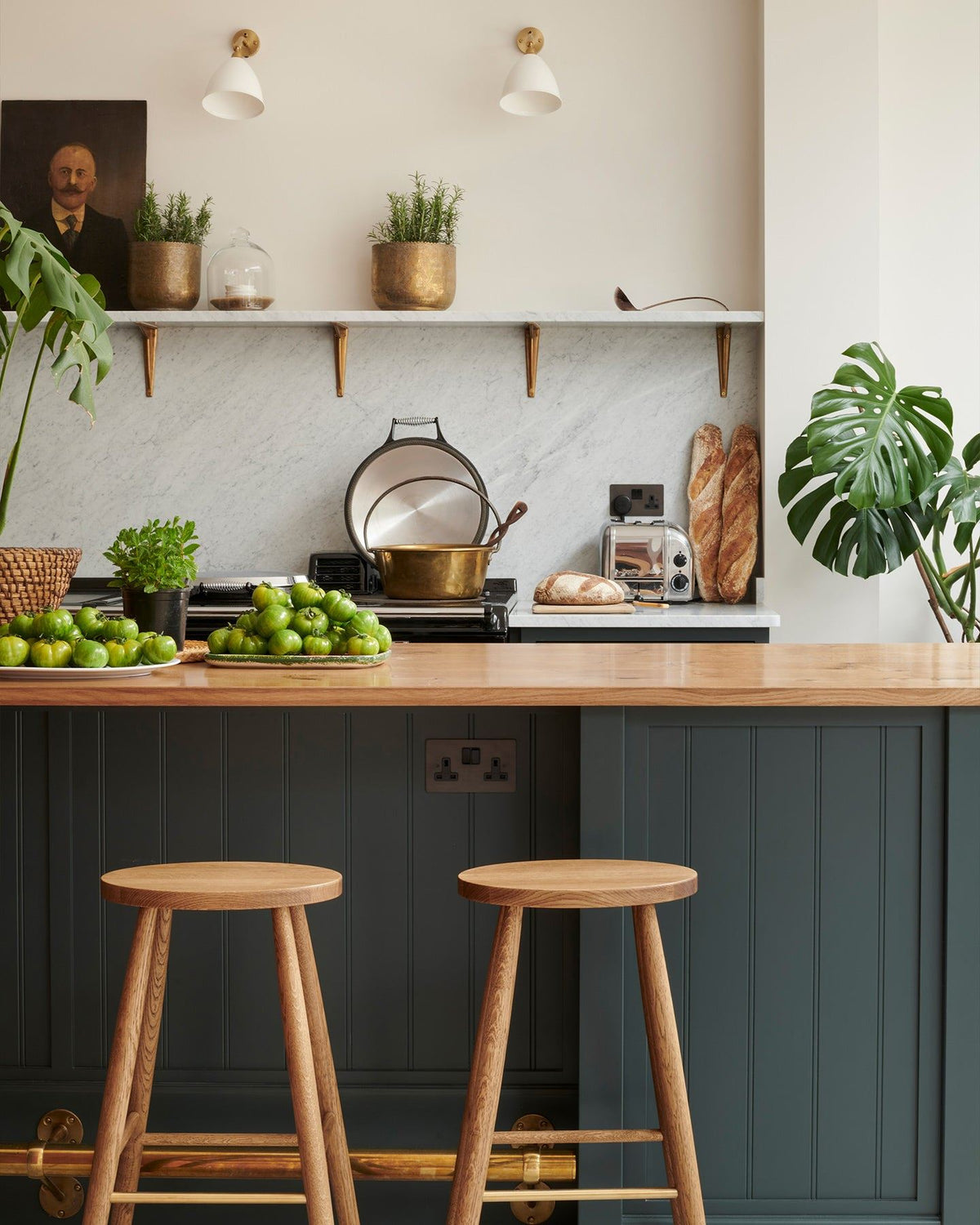 A dark green painted Shaker-style kitchen with a breakfast bar island, simple oak bar stools and a Carrara marble splashback. TEST