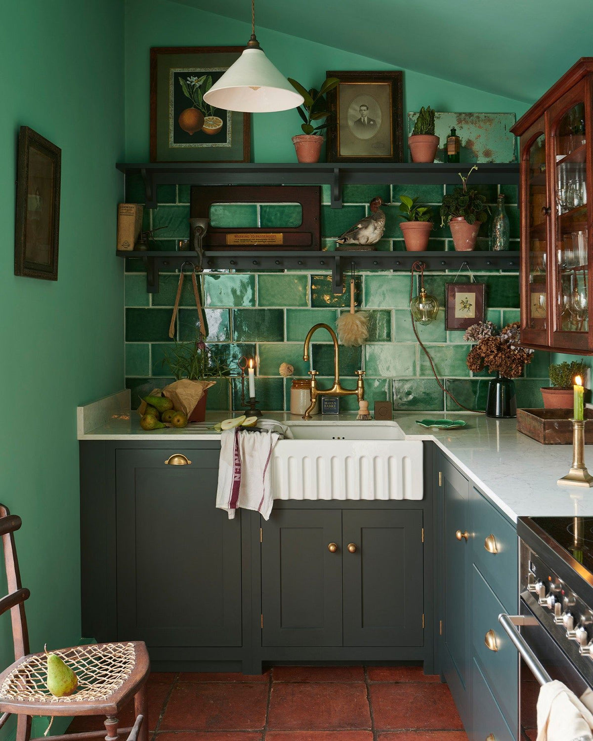 An eclectic cottage kitchen with dark green painted Shaker-style cupboards, arsenic green walls, glossy emerald green wall tiles, vintage bric-a-brac and a terracotta tiled floor. TEST