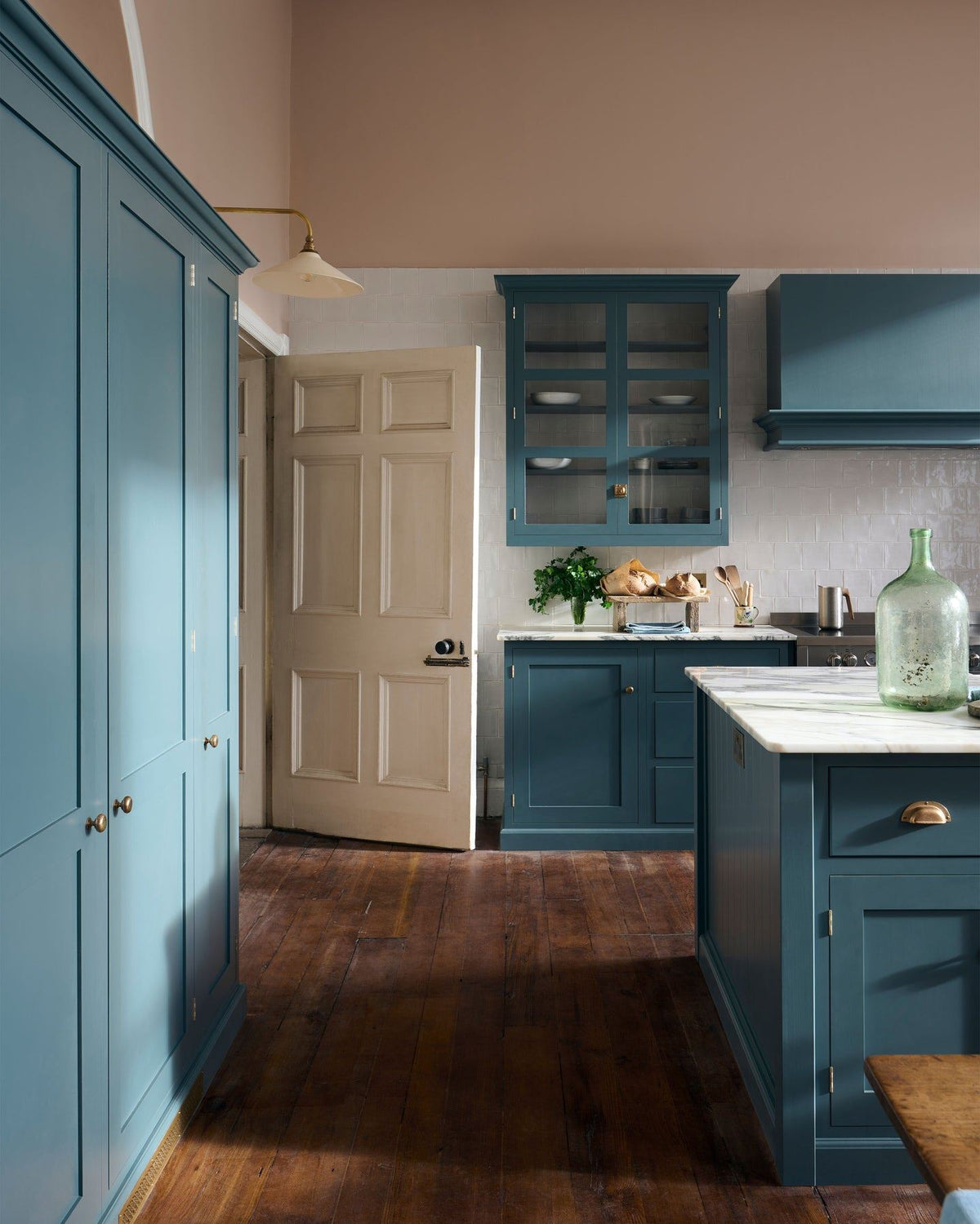 An impressive room with high ceilings, plaster pink walls, rich worn floorboards and a green-blue painted Shaker-style kitchen. TEST
