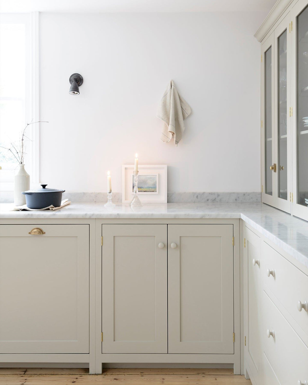 A simple Shaker-style kitchen corner with creamy mushroom coloured cupboards, white walls, a Carrara marble worktop and a lit candle. TEST