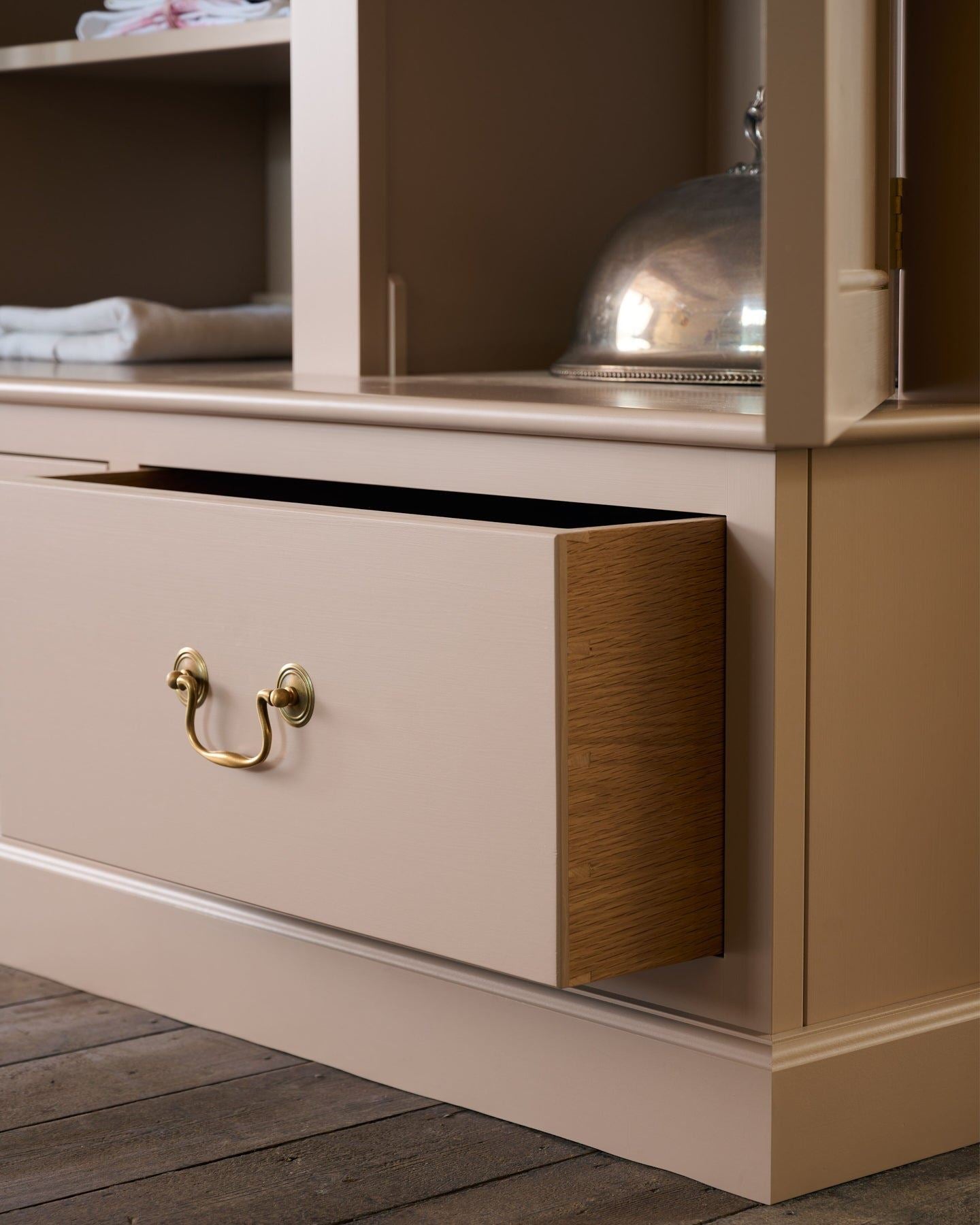 A close-up oblique view of a soft pink coloured oak drawer box with dovetailed joinery and a Georgian-style swing handle in a tarnished silver finish.