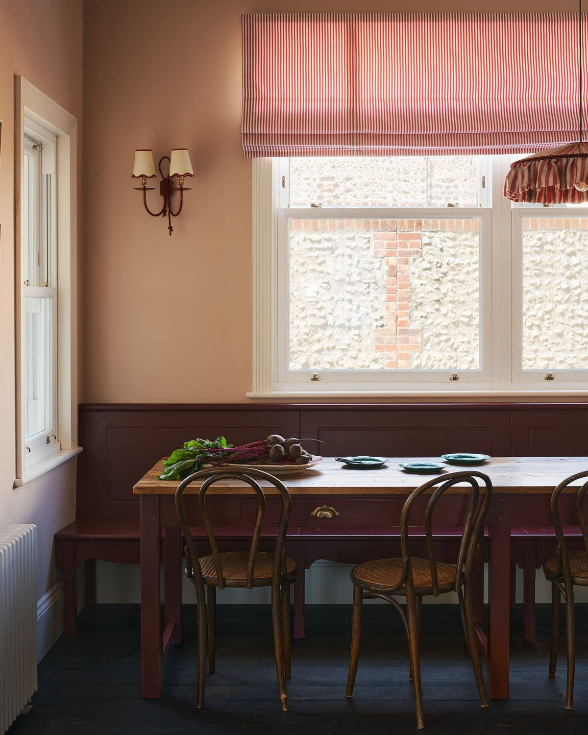 A straight-on view of a long banquet-style dining table with a reclaimed pine top and red painted frame and legs. A red painted fitted bench seat can be seen behind the table. TEST