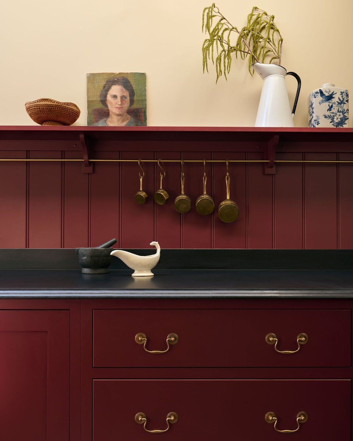A close-up view of red painted Shaker-style kitchen drawers with a black granite worktop and red tongue and groove panelling above. TEST