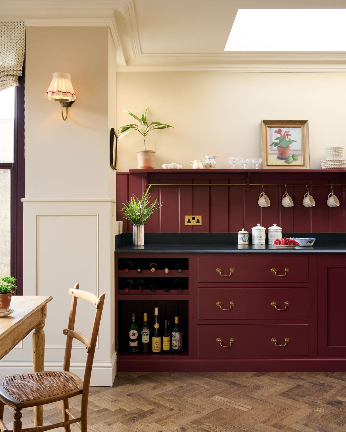 A straight-on view of a red painted Shaker-style kitchen with parquet wood flooring, cream walls, a black granite worktop and red tongue and groove panelling above. TEST