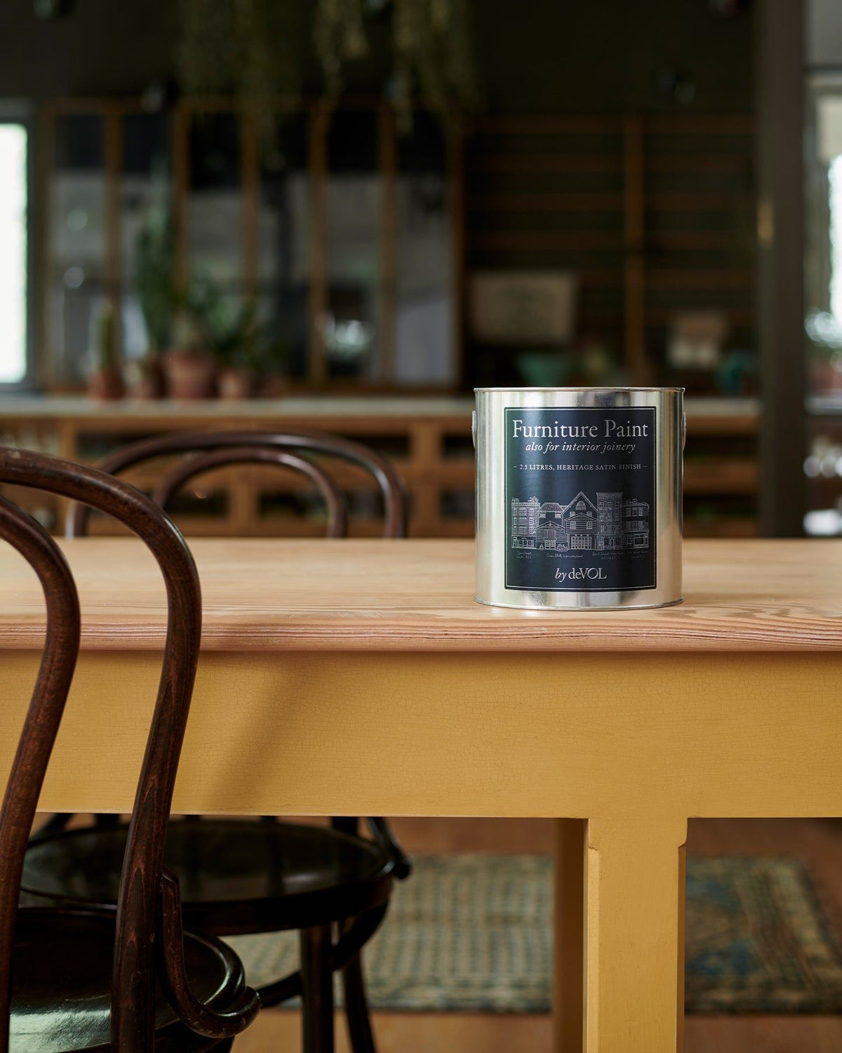 A close-up view of a silver paint tin with a blue label on a yellow painted prep table with a smooth pine tabletop. TEST