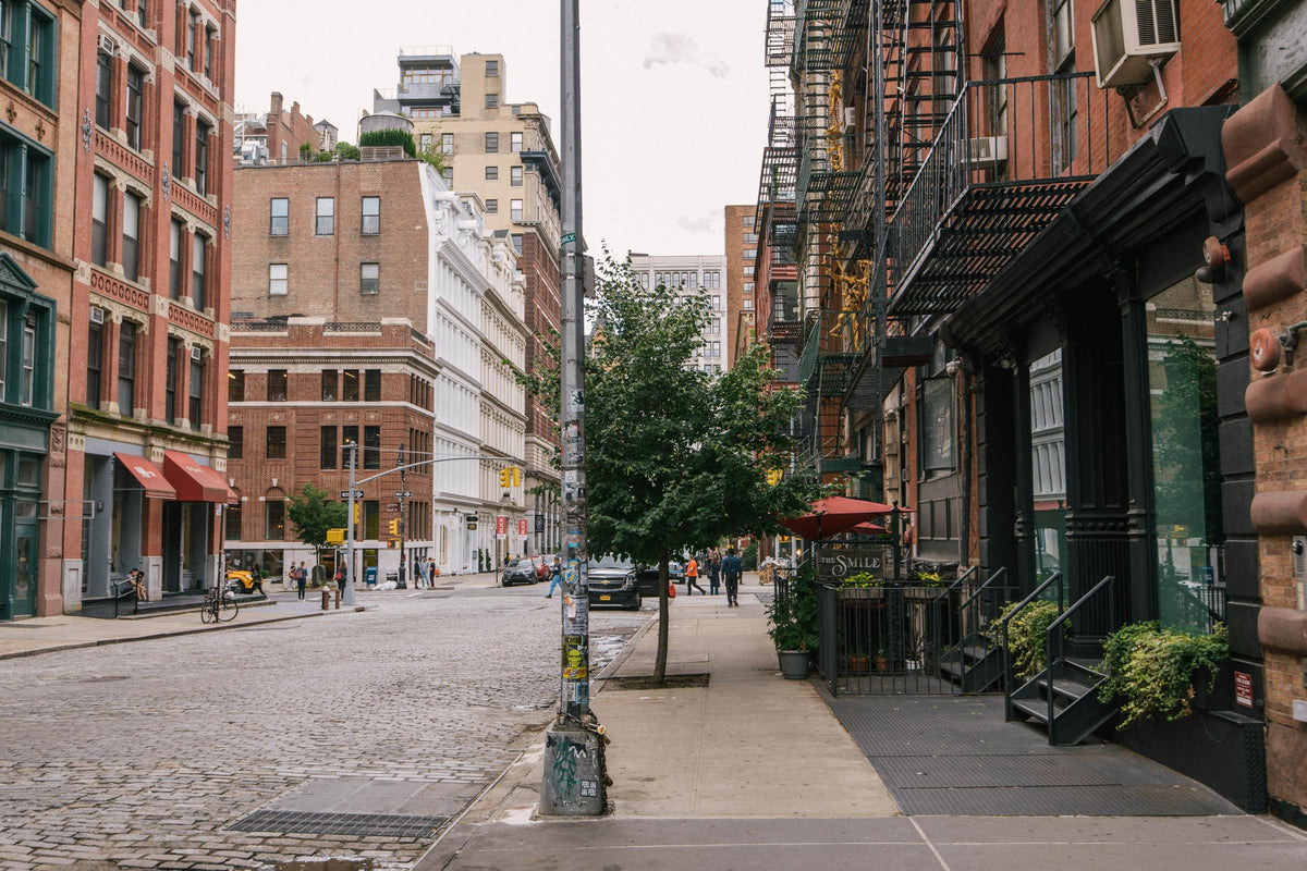 A scenic New York City street, with tall red bricked buildings, steel fire escapes, cobbled stone roads, and to the right is the deVOL Bond Street New York City showroom.