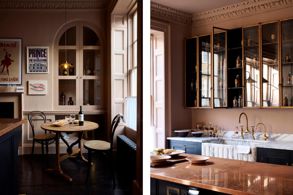 A bold and dramatic Haberdasher’s kitchen with a sink and cooker run, an Arabescato worktop and single fluted sink, an aged brass Ionian tap, a glazed wall cupboard, a kitchen island with a copper worktop, a deVOL petite vineyard table, Bentwood café chairs, and a petite frilly chartreuse light. Adorned with artisan ceramics, labelled glass jars, and a colourful sandwich, creating a local bristo bar in a Manhattan space.