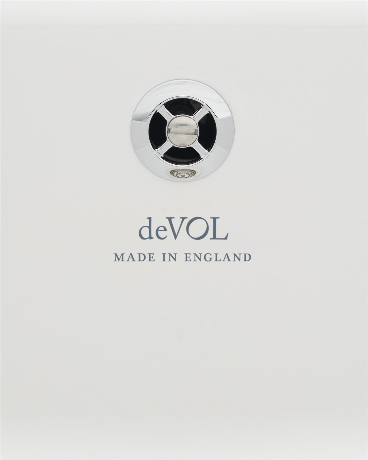 A close-up view of a circular sink overflow cap in a polished chrome finish fitted to a ceramic sink. A logo on the ceramic sink below reads 'deVOL; Made in England'. TEST