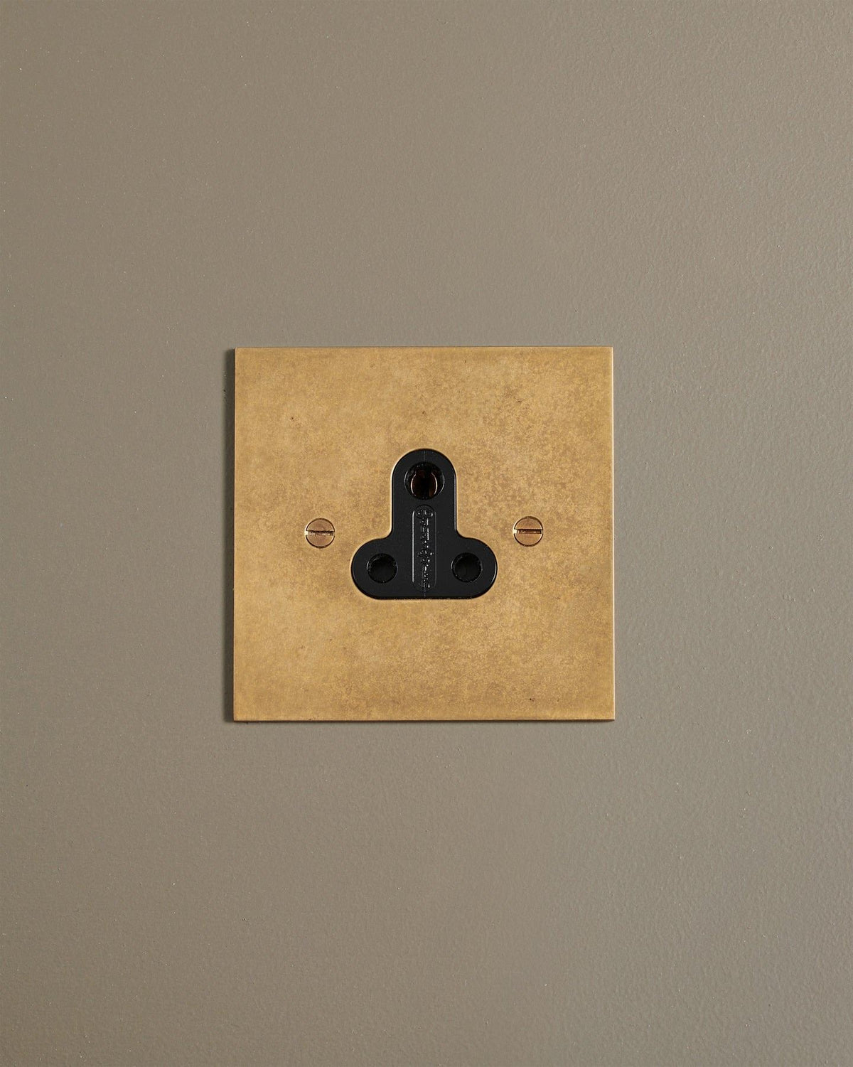 A straight-on view of a classic 5 amp single plug socket in a mottled aged brass finish. TEST