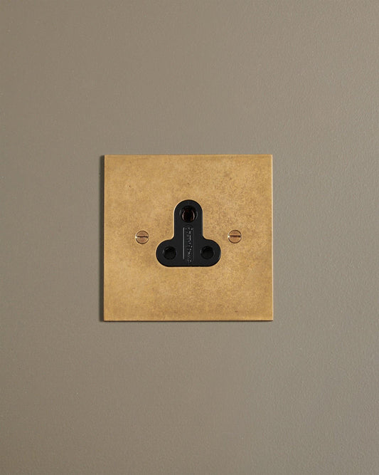 A straight-on view of a classic 5 amp single plug socket in a mottled aged brass finish.