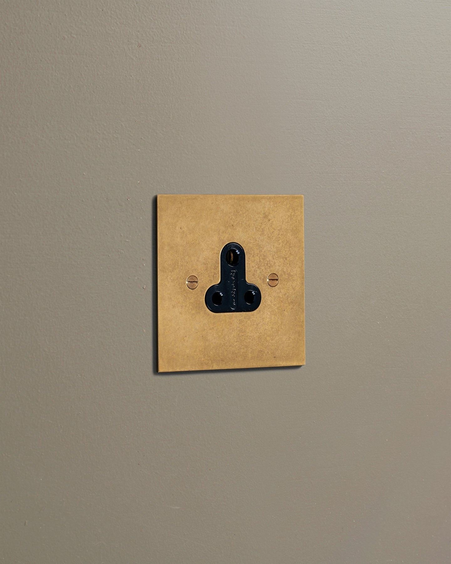 An oblique view of a classic 5 amp single plug socket in a mottled aged brass finish.