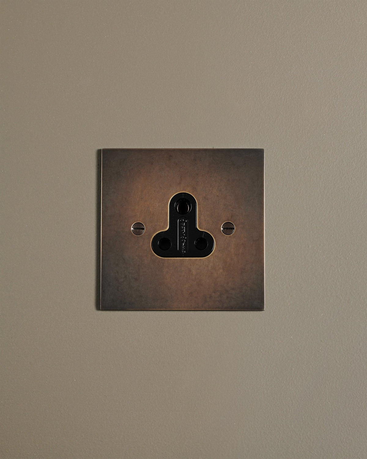 A straight-on view of a classic 5 amp single plug socket in a dark oxidised brass finish. TEST