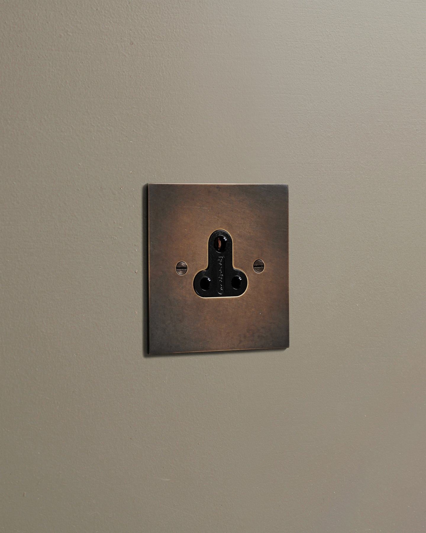 An oblique view of a classic 5 amp single plug socket in a dark oxidised brass finish.