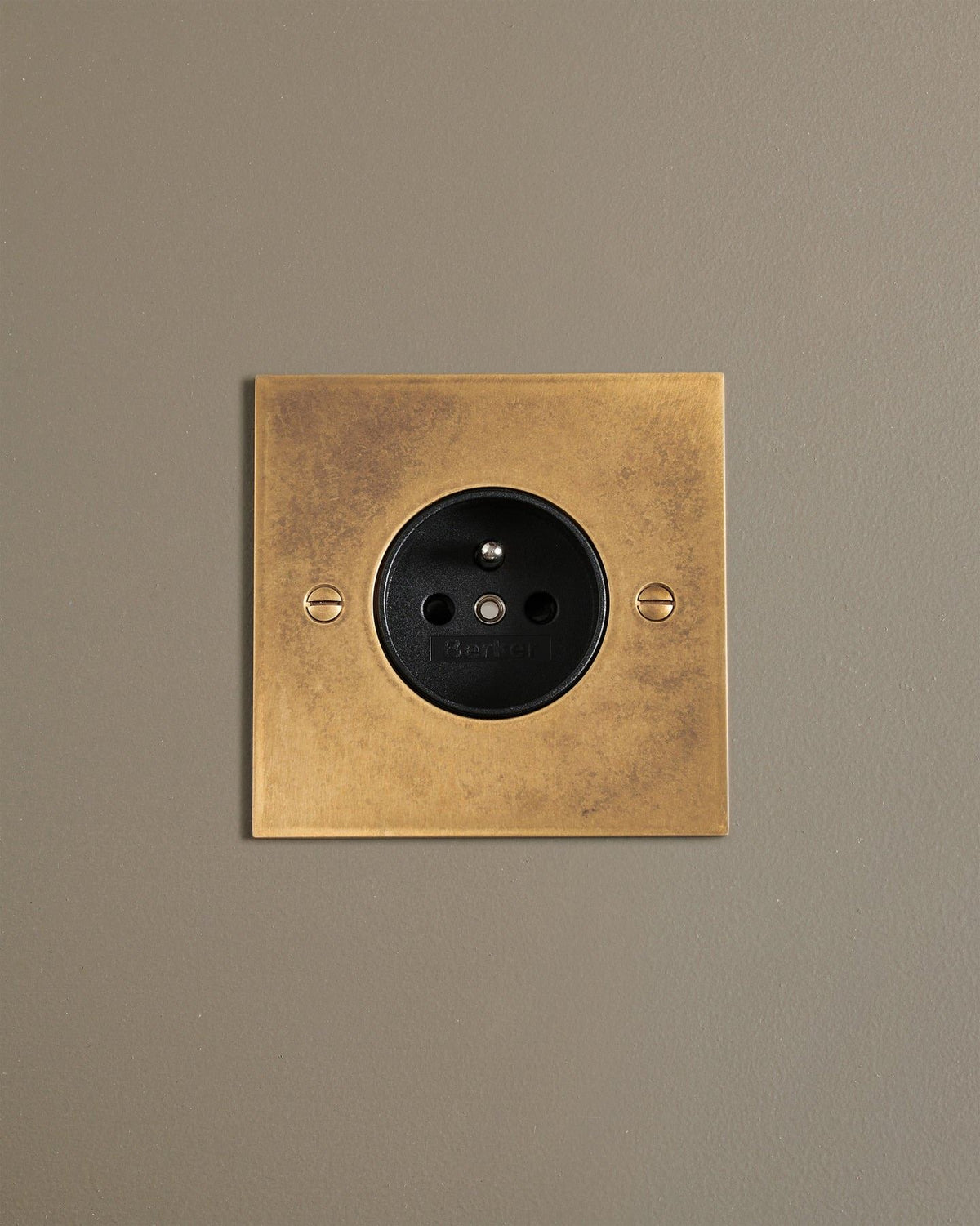 A straight-on view of a classic French-style single plug socket in a mottled aged brass finish. TEST
