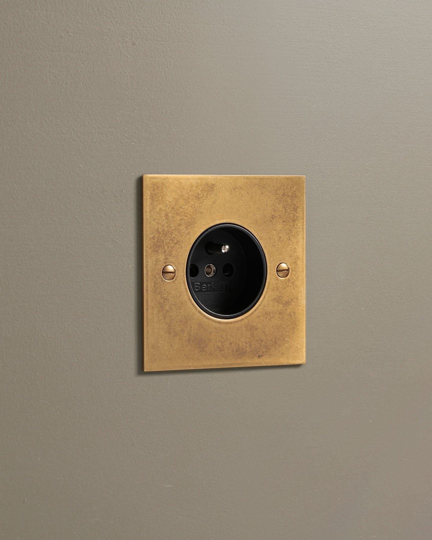 An oblique view of a classic French-style single plug socket in a mottled aged brass finish.