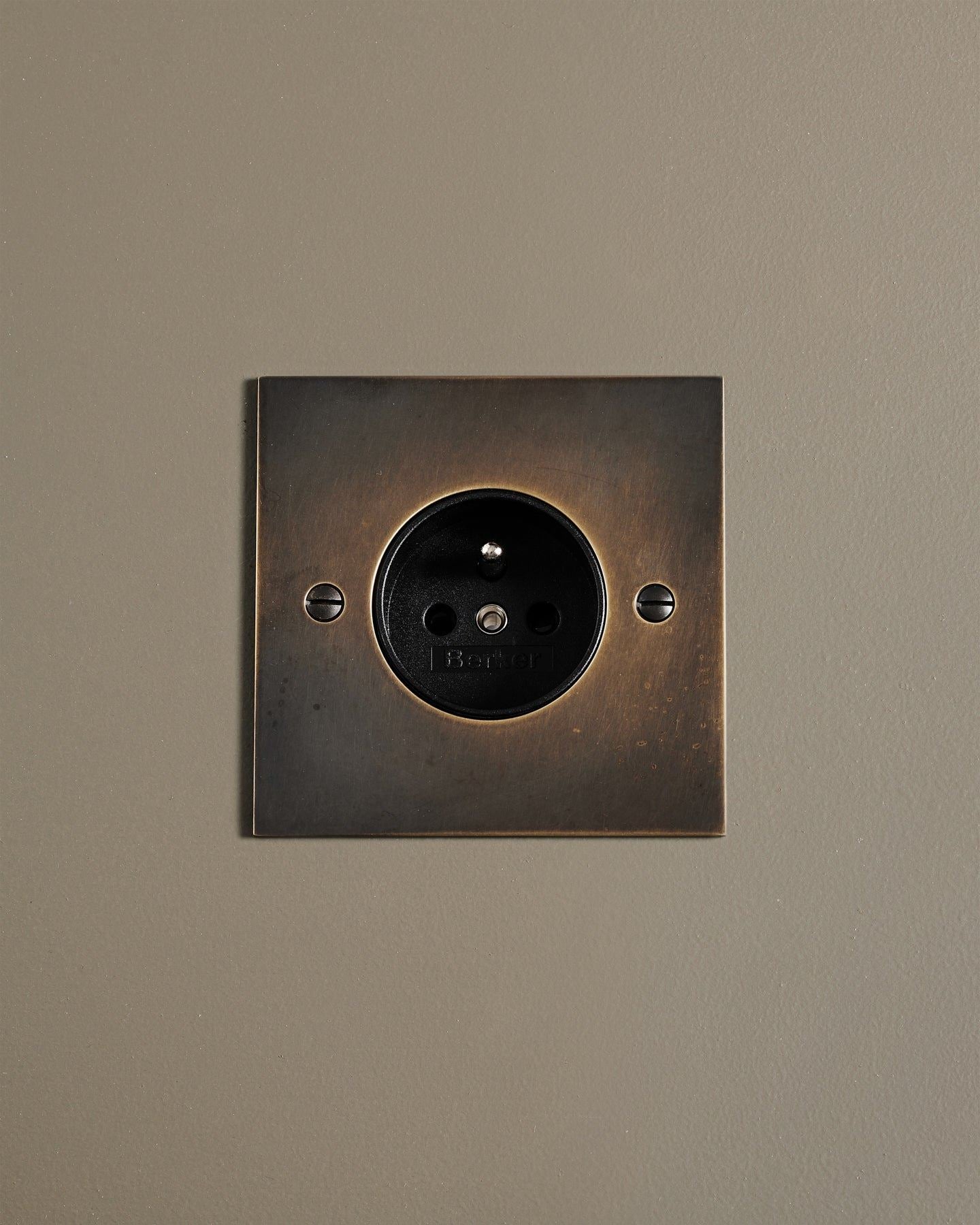 A straight-on view of a classic French-style single plug socket in a dark oxidised brass finish.