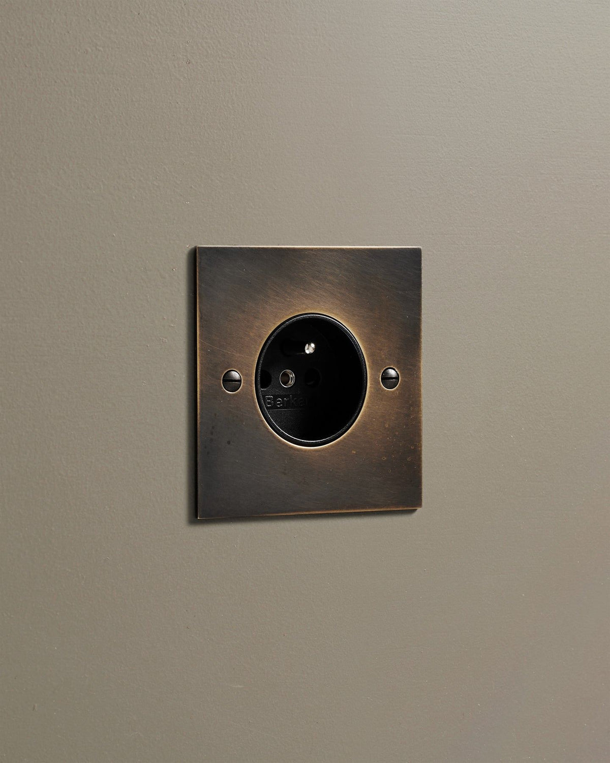 An oblique view of a classic French-style single plug socket in a dark oxidised brass finish. TEST