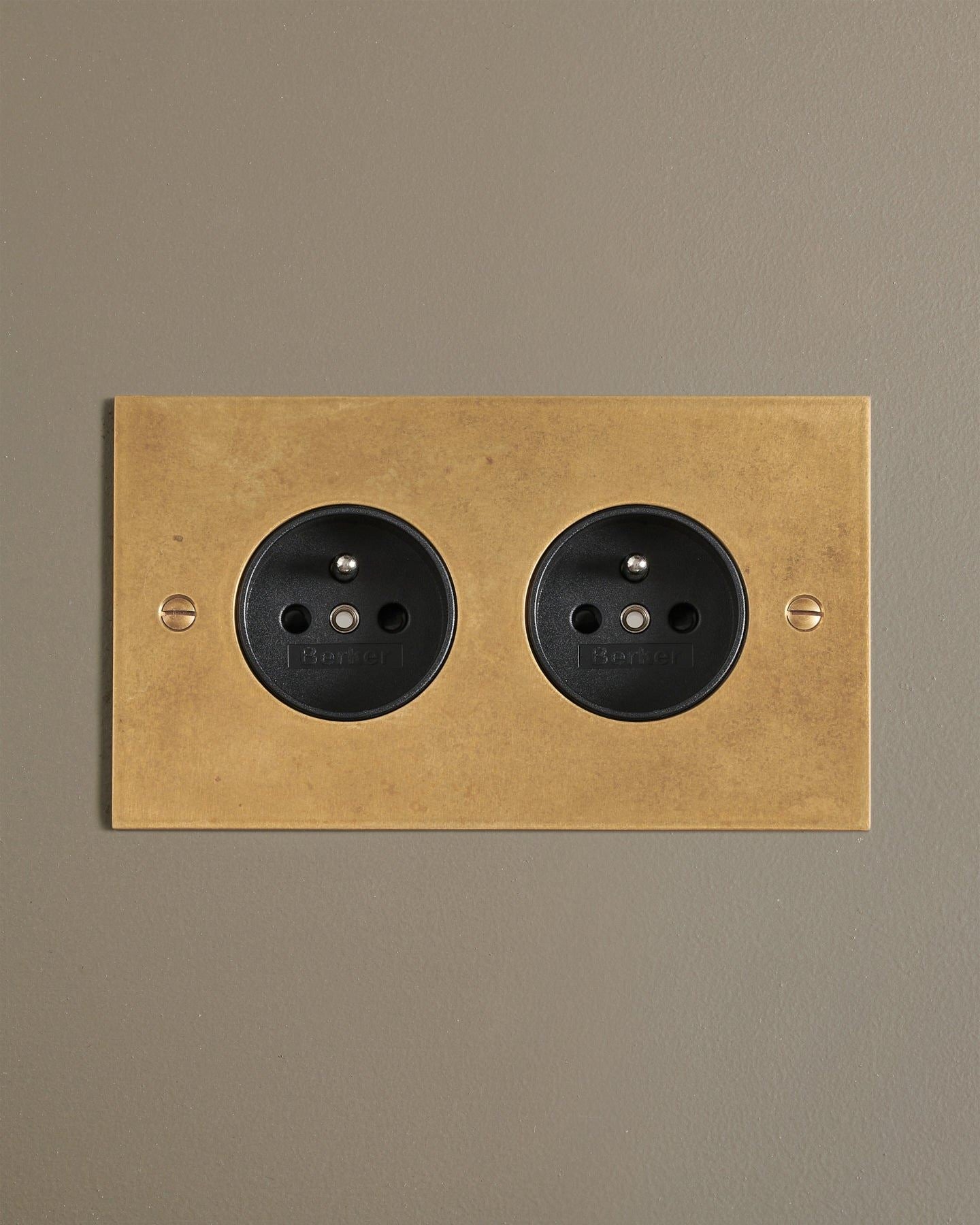 A straight-on view of a classic French-style twin plug socket in a mottled aged brass finish.