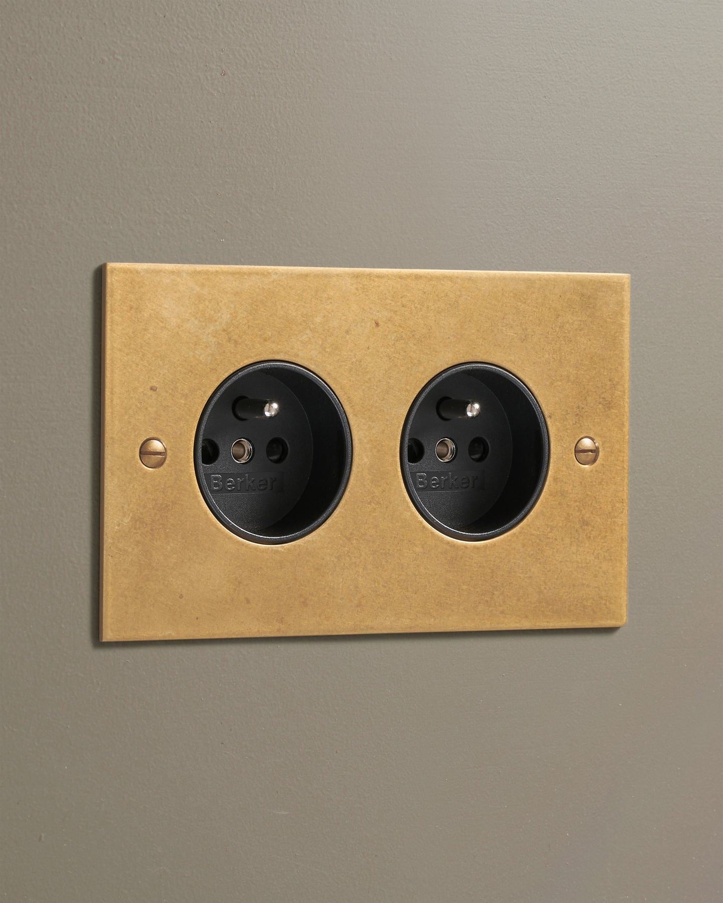 An oblique view of a classic French-style twin plug socket in a mottled aged brass finish.