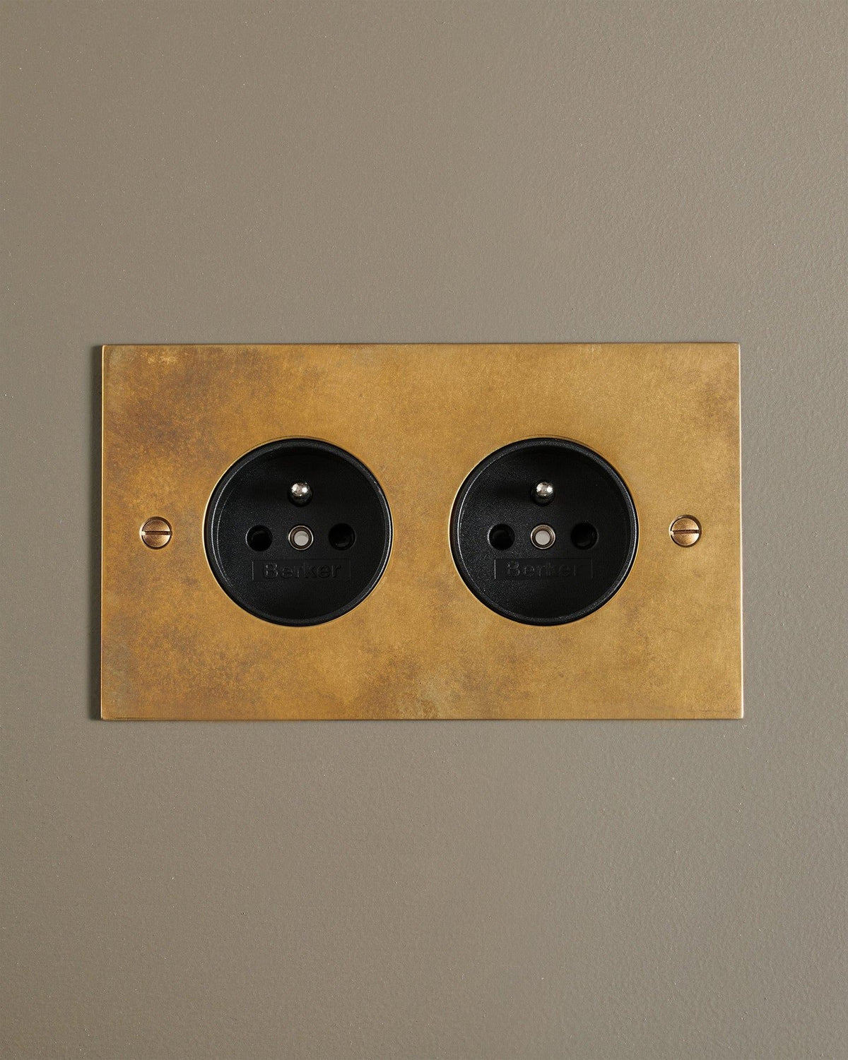 A straight-on view of a classic French-style twin plug socket in a warm burnished brass finish. TEST