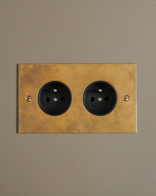 A straight-on view of a classic French-style twin plug socket in a warm burnished brass finish.