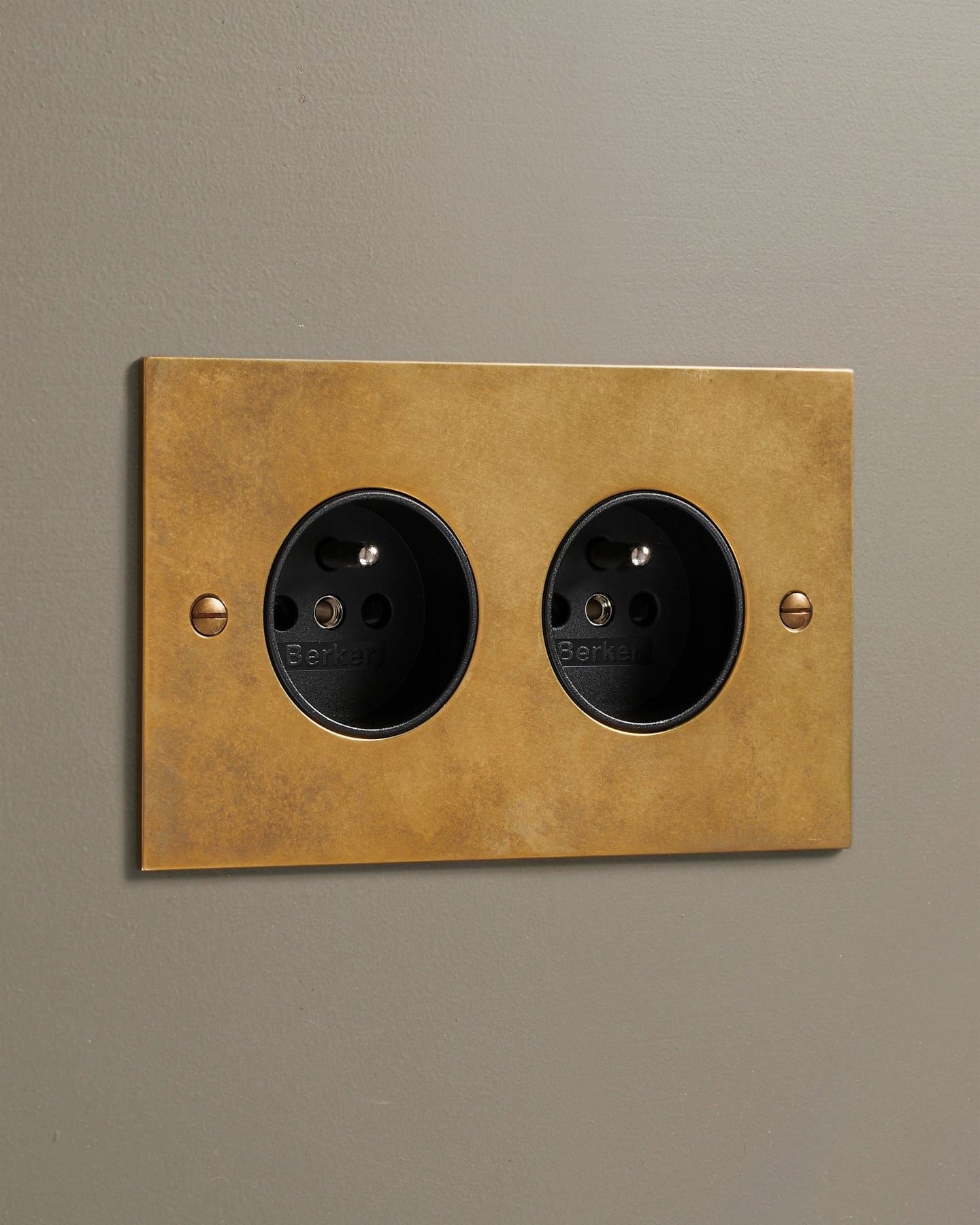 An oblique view of a classic French-style twin plug socket in a warm burnished brass finish.