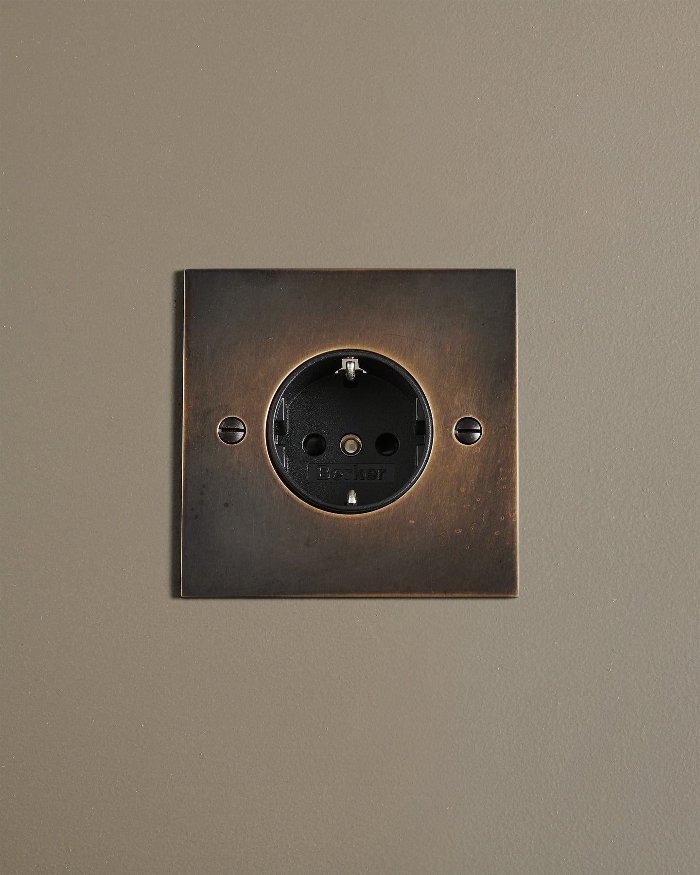 A straight-on view of a classic Schuko-style single plug socket in a dark oxidised brass finish.