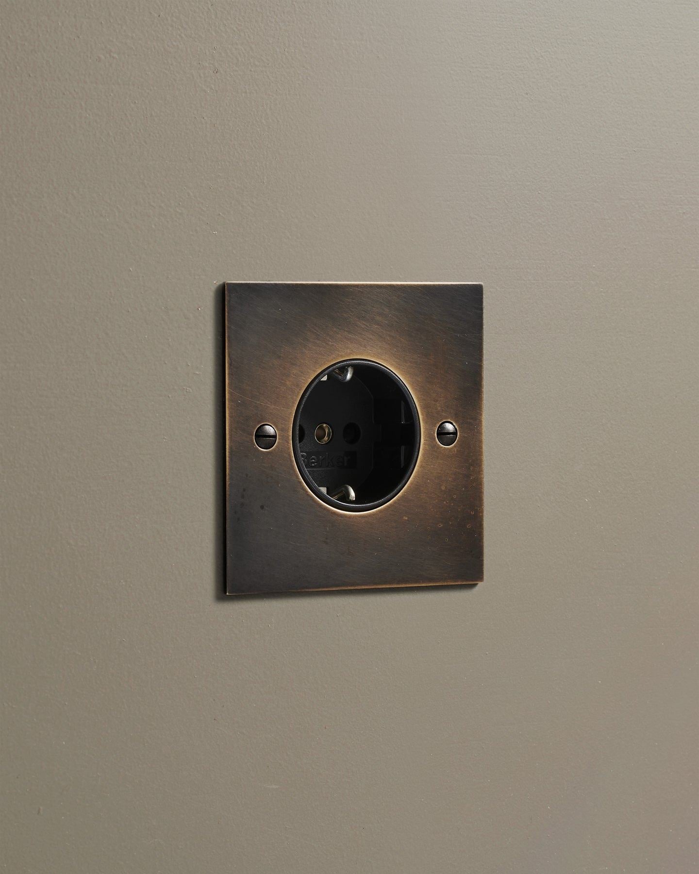 An oblique view of a classic Schuko-style single plug socket in a dark oxidised brass finish.