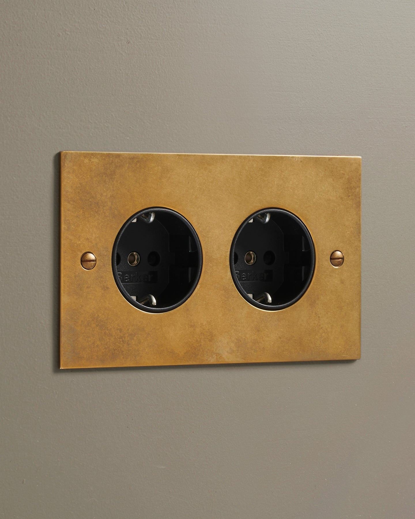 An oblique view of a classic Schuko-style twin plug socket in a warm burnished brass finish.