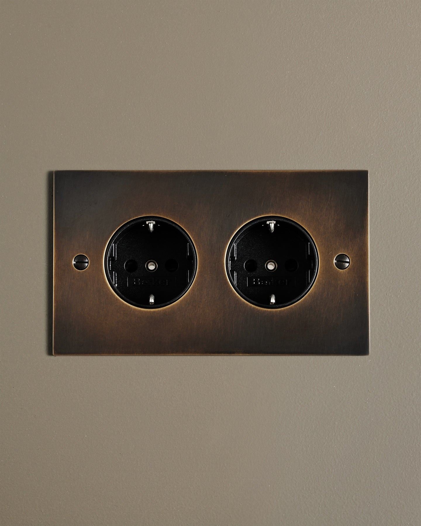 A straight-on view of a classic Schuko-style twin plug socket in a dark oxidised brass finish.