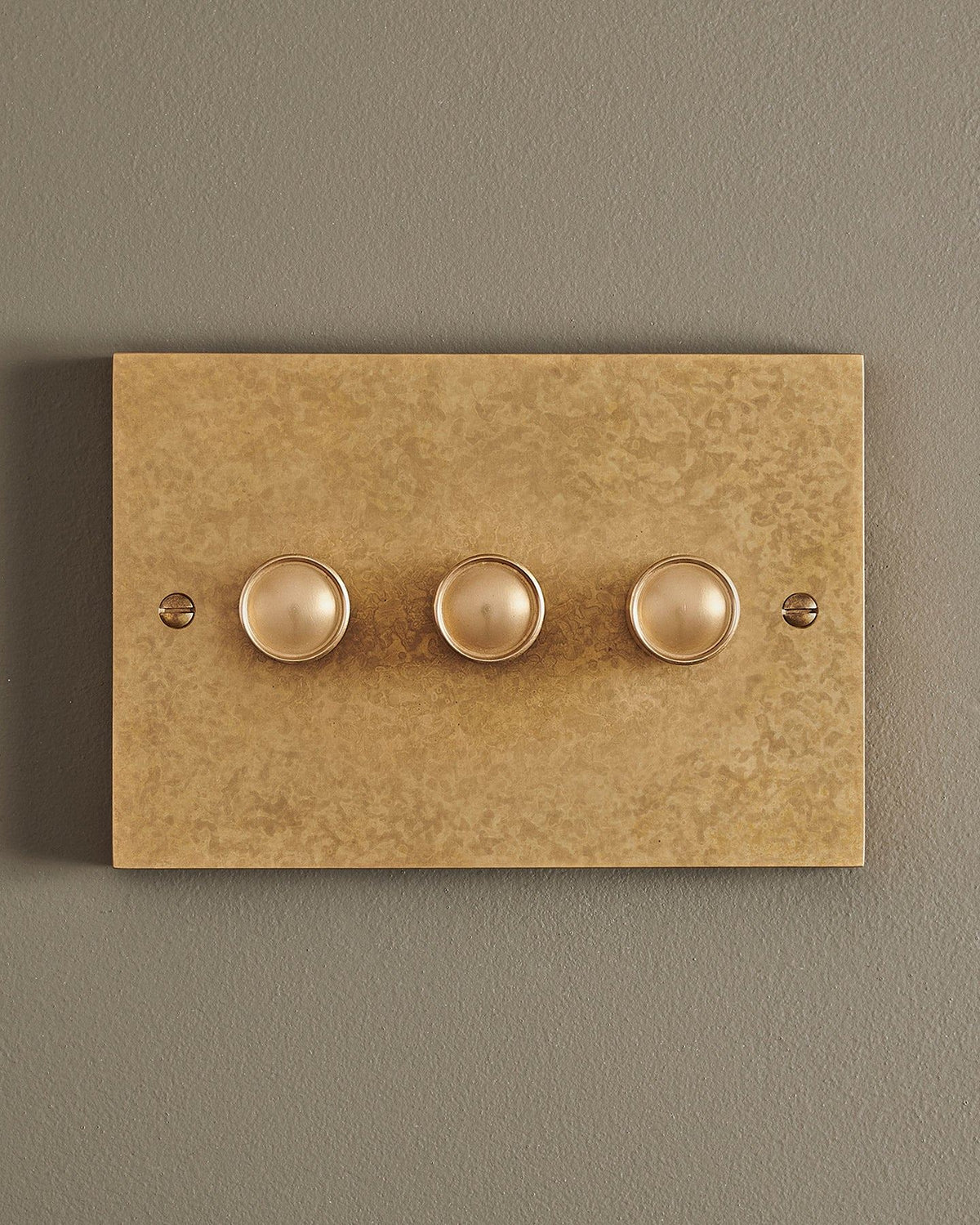 A straight-on view of a 3 gang box dimmer switch in a mottled aged brass finish. TEST