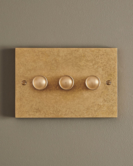 A straight-on view of a 3 gang box dimmer switch in a mottled aged brass finish.