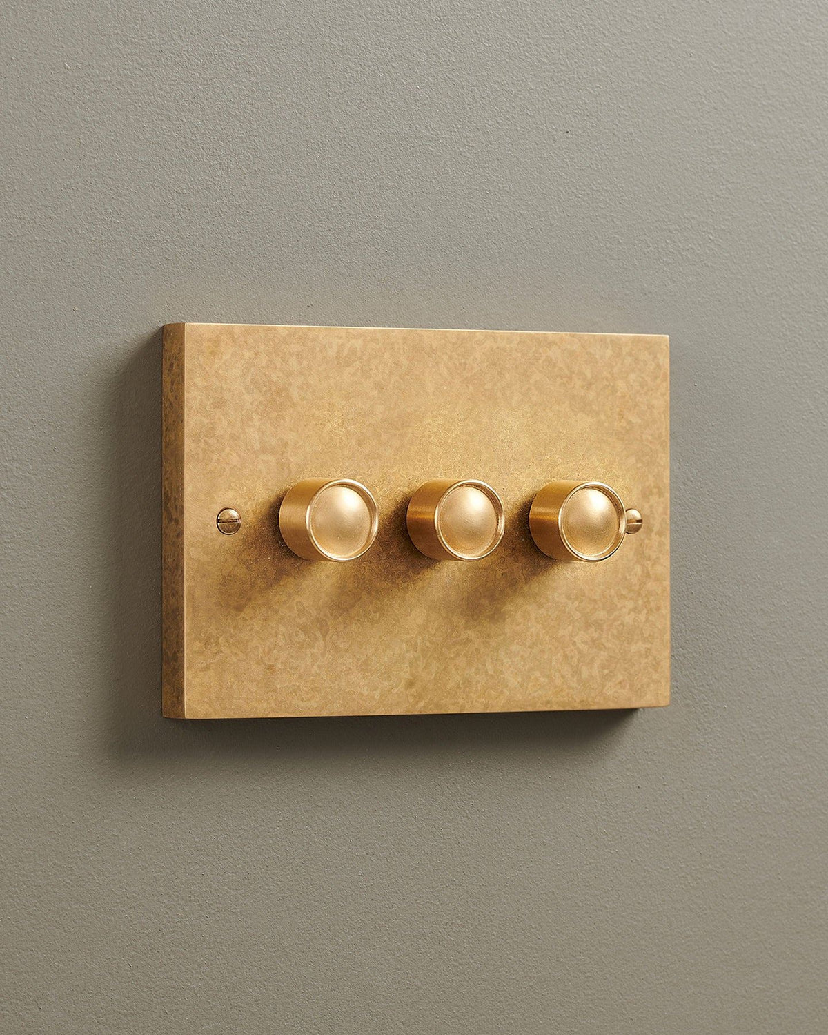 An oblique view of a 3 gang box dimmer switch in a mottled aged brass finish. TEST