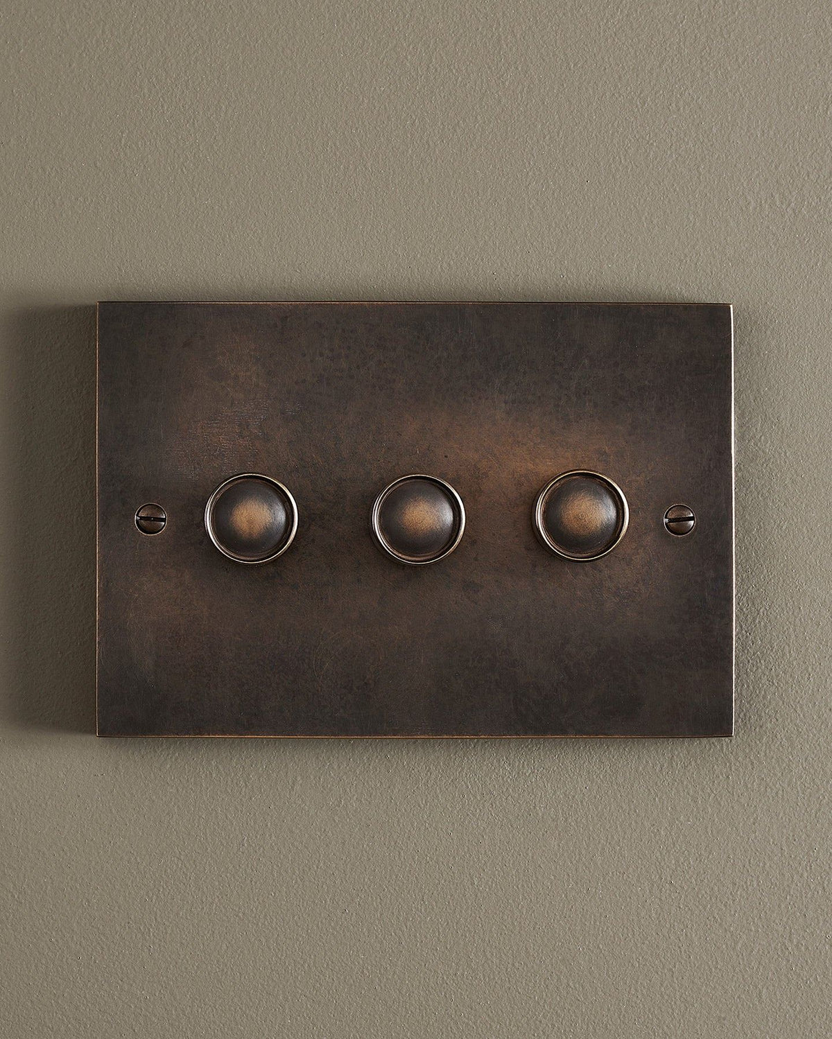 A straight-on view of a 3 gang box dimmer switch in a dark oxidised brass finish. TEST