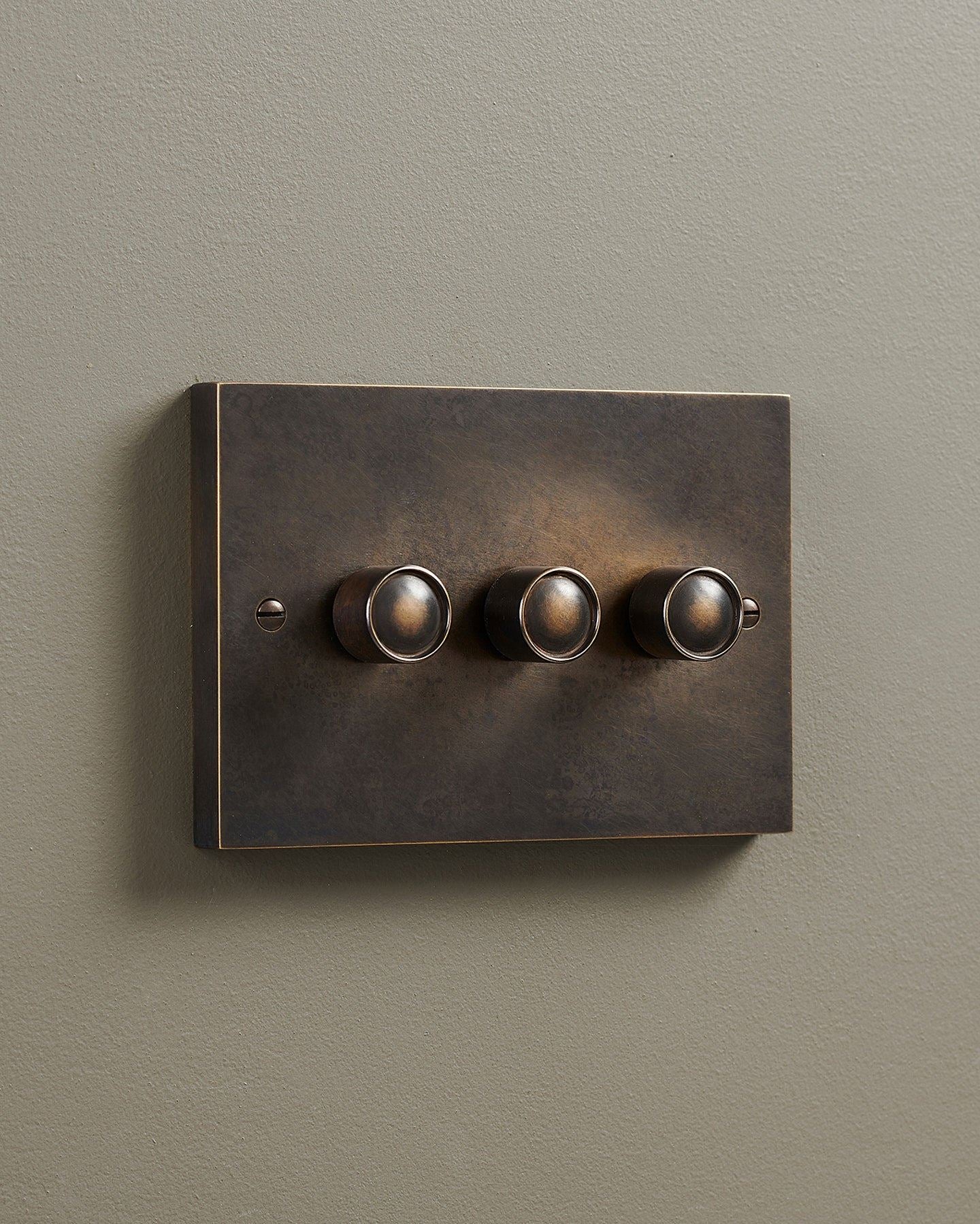 An oblique view of a 3 gang box dimmer switch in a dark oxidised brass finish.