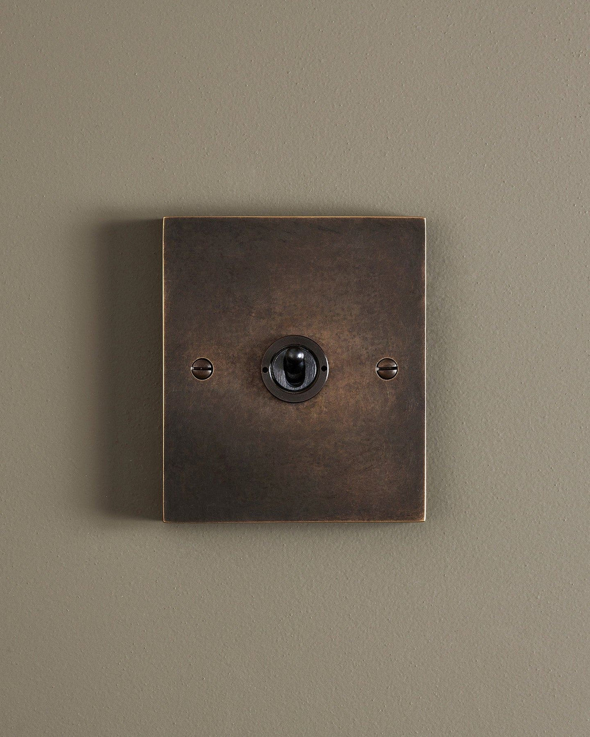 A straight-on view of a 1 gang box toggle switch in a dark oxidised brass finish. TEST