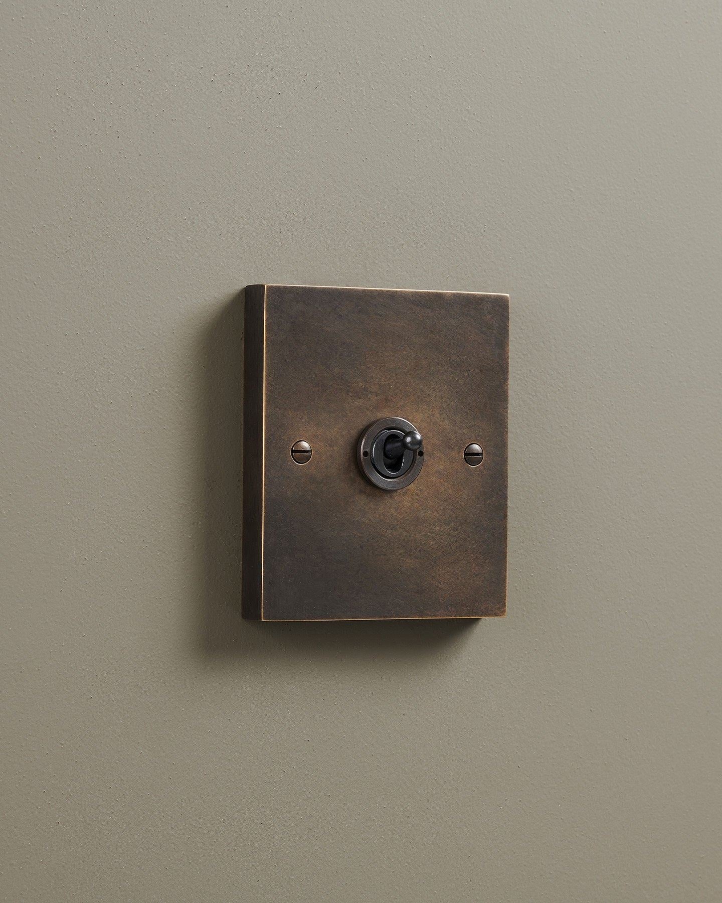 An oblique view of a 1 gang box toggle switch in a dark oxidised brass finish.