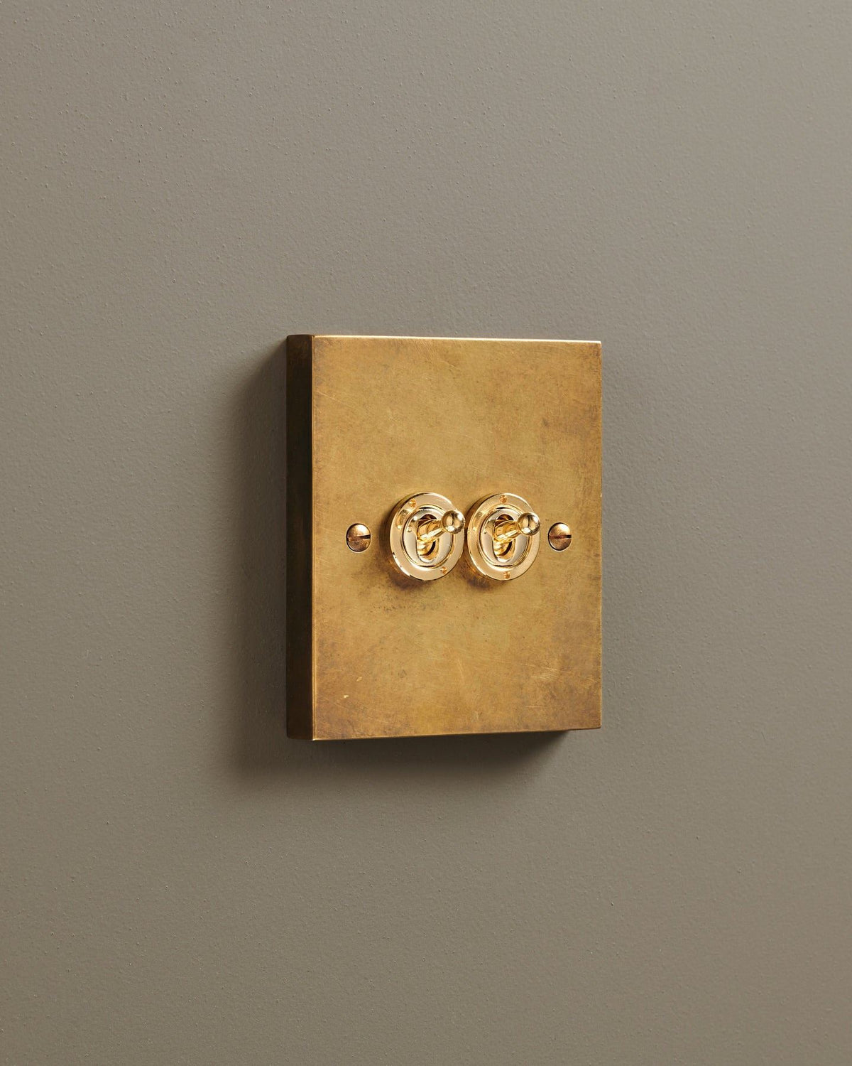 An oblique view of a 2 gang box toggle switch in a warm burnished brass finish. TEST