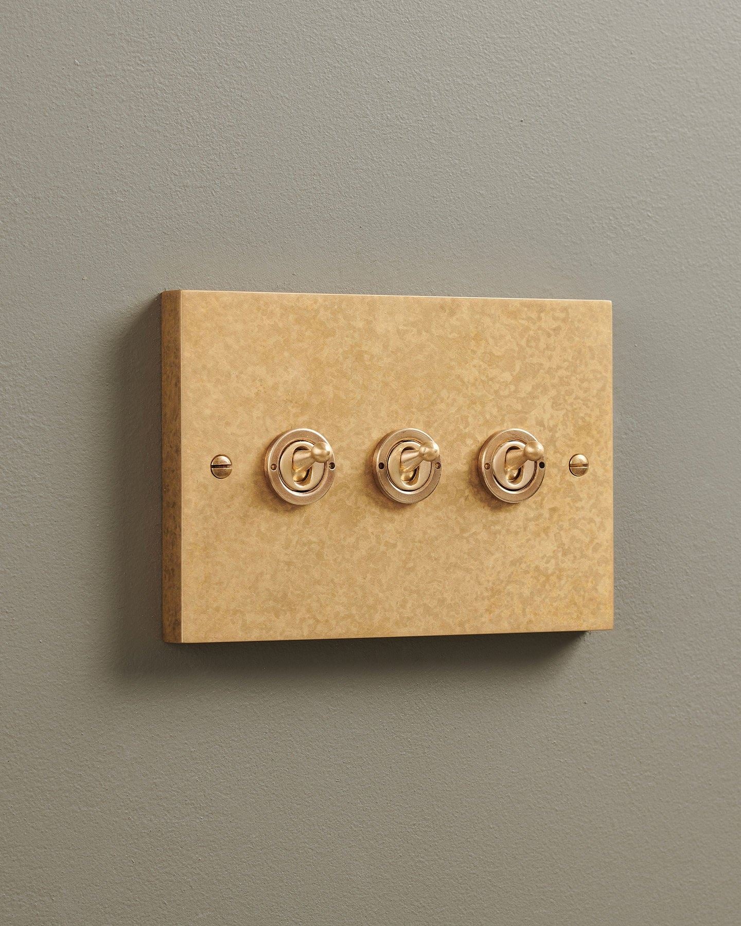 An oblique view of a 3 gang box toggle switch in a mottled aged brass finish.
