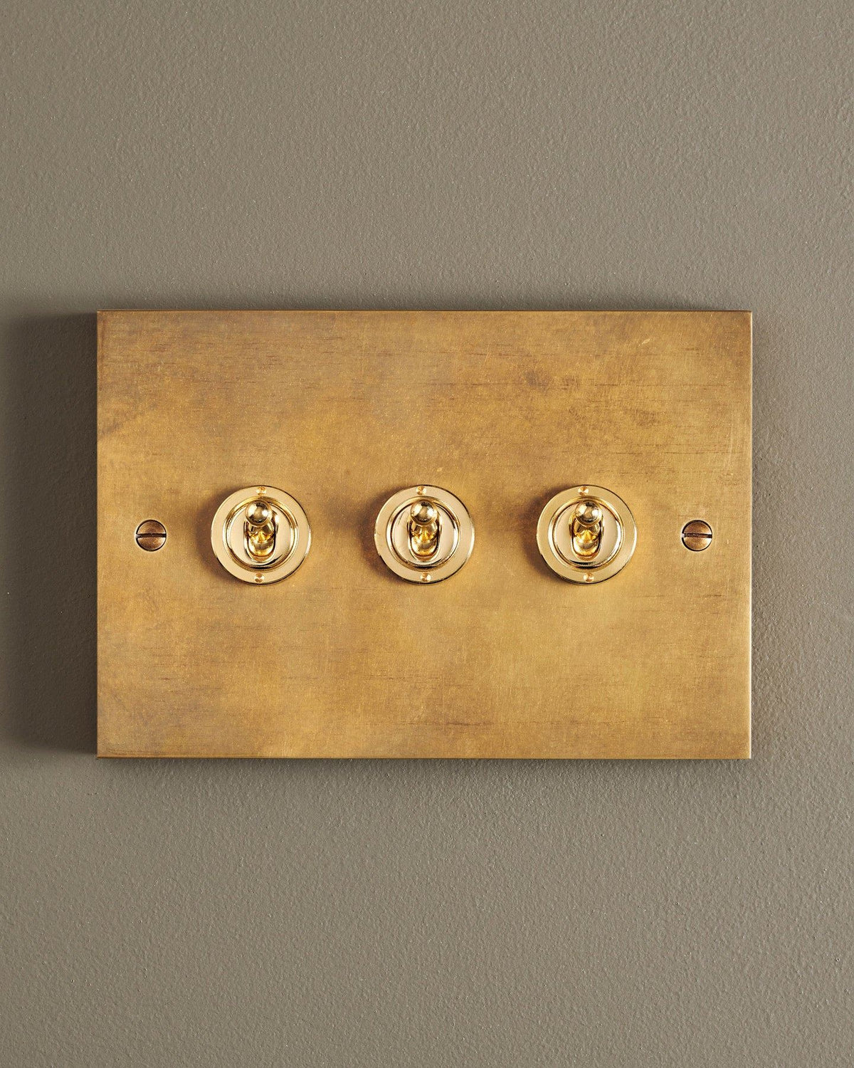 A straight-on view of a 3 gang box toggle switch in a warm burnished brass finish. TEST